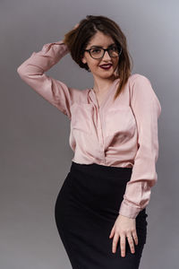 Portrait of young woman standing against gray background