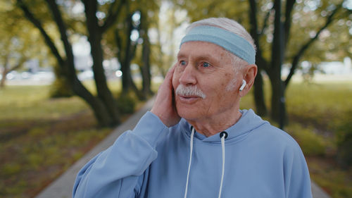 Senior man talking through wireless in ear headphones at park