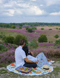 Rear view of woman sitting on field against sky