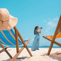 Tilt image of woman standing on beach against blue sky