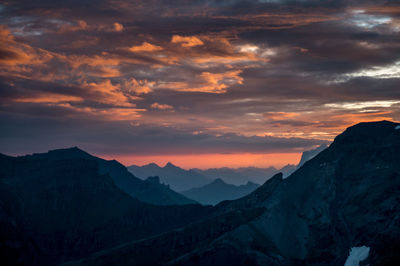 Scenic view of silhouette mountains against dramatic sky during sunset