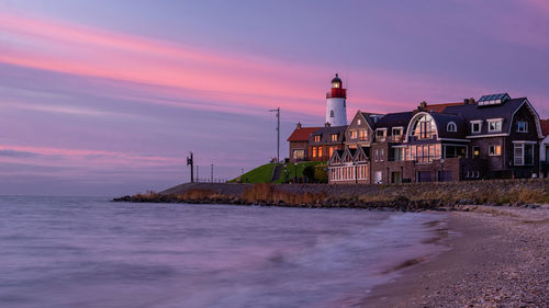 Lighthouse by sea against sky during sunset