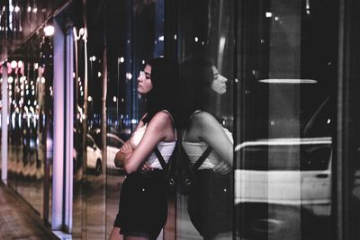 Young woman leaning on glass wall at night