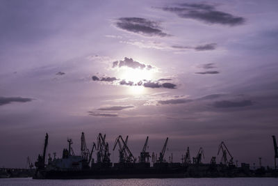 Silhouette cranes at commercial dock against sky during sunset