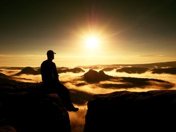 Moment of loneliness. man with cap sit on the peak of rock and thinking. dreamy autumn ladscape