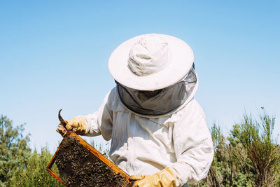 Beekeeper working on beehive while standing against sky