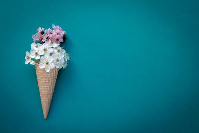 Close-up of ice cream cone with flowers against blue background