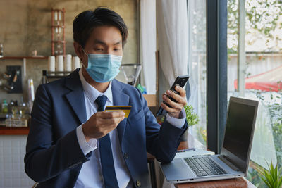 Businessman wearing mask holding credit card at cafe