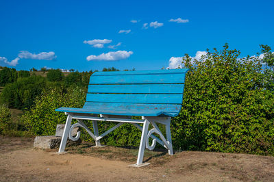 Empty bench and table against trees against blue sky