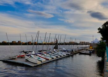 Sailboats moored at harbor against sky during sunset