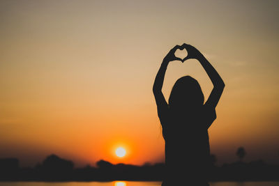 Silhouette woman making heart shape with hands against sky during sunset