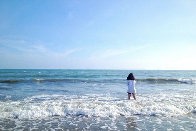 Rear view of man standing at beach against clear sky