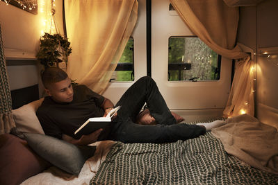 Man reading book on bed in camper van