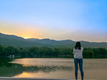 Rear view of woman standing on mountain against sky during sunset