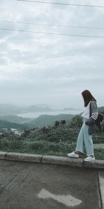 Side view of woman walking on retaining wall against landscape and cloudy sky