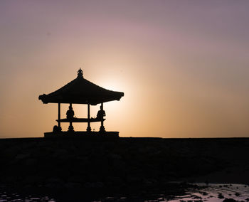Silhouette cross on shore against sky during sunset