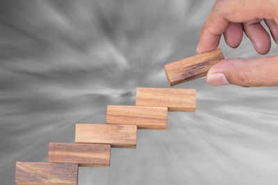 Cropped hand of man stacking wooden toy blocks against cloudy sky