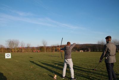 Rear view of men shooting arrows on field against sky