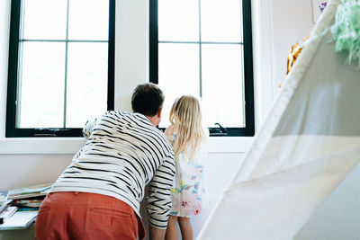 View from behind of a father and daughter looking out a window