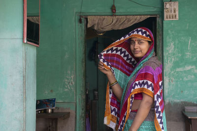 Portrait of indian woman covering her face with sari standing at entrance of building