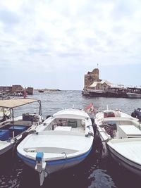 Boats moored in sea against cloudy sky