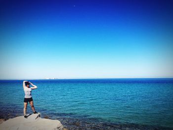 Rear view of man looking at sea against clear sky