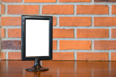 Close-up of picture frame on table by brick wall