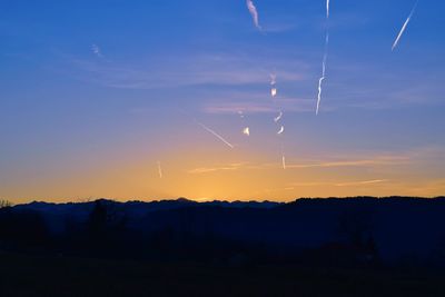 Silhouette landscape against vapor trails in sky during sunset