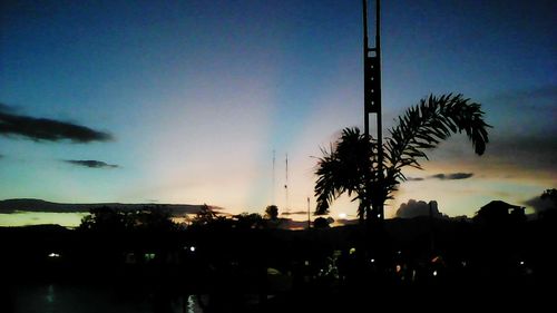 Silhouette of palm trees against cloudy sky