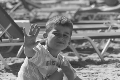 Portrait of smiling boy gesturing while sitting on sand at beach