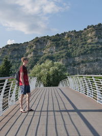 Side view of man with backpack standing on bridge against mountain