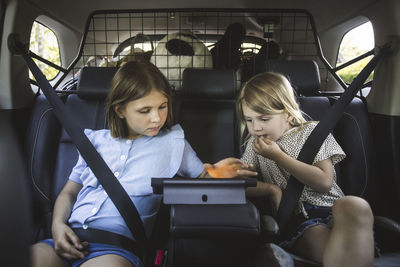 Portrait of mother, father and two daughters standing by car at electric vehicle charging station