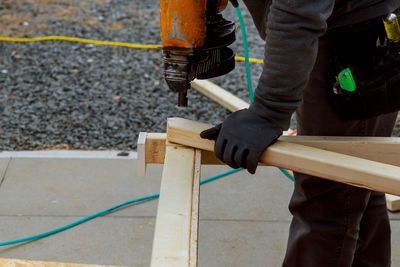 Midsection of man using nail gun on woods at construction site
