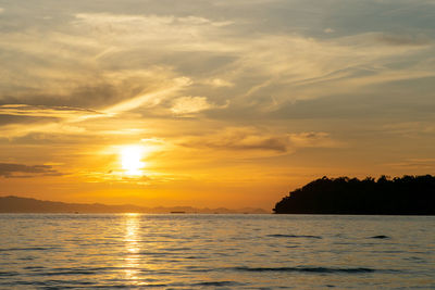 Landscape of calm sea with silhouette of island and orange light of sunrise