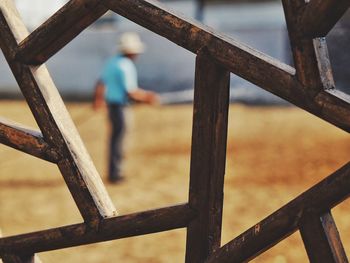 Close-up of wooden fence with man standing in background at beach