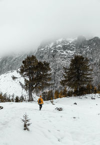 Rear view of female hiker walking on snowy path under amazing misty mountains