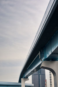 Low angle view of bridge by buildings against sky