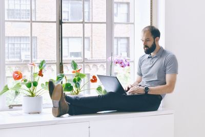 Man using laptop while sitting by window at home