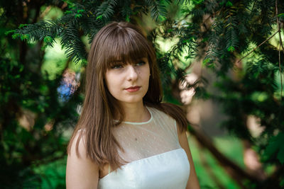 Portrait of beautiful young woman standing against trees