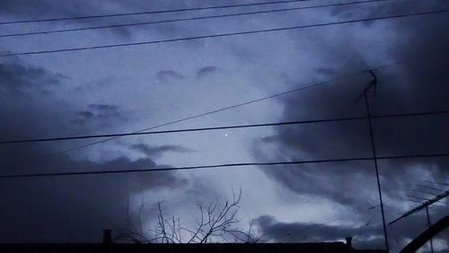 Low angle view of electricity pylon against cloudy sky