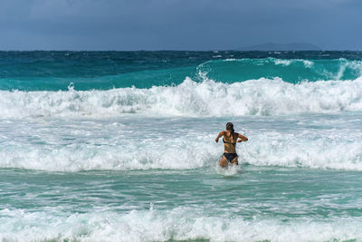 Woman standing in sea with waves on tropical beach with turquoise ocean