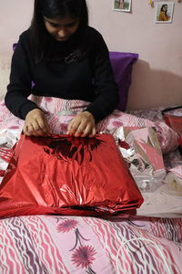 Midsection of woman sitting on bed at home