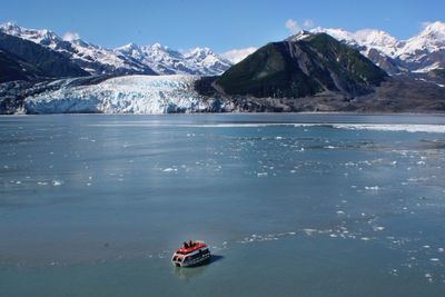 Boat sailing in river by snow covered mountains against sky