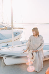 Happy young woman in dress and hat walks on the beach near the boats