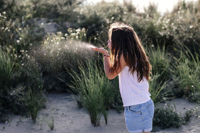 Girl blowing while standing on sand during sunny day