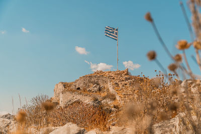 Greek flag flapping in wind atop rocky hill in hydra greece with copyspace.