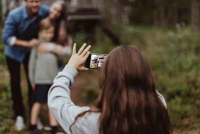 Girl taking picture of family with mobile phone while standing in backyard