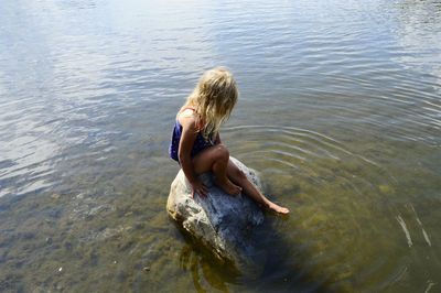 Side view of girl sitting on rock in lake