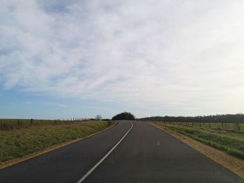 Empty road amidst field against sky