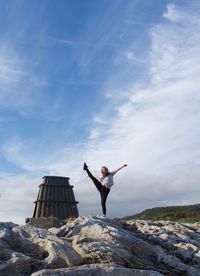 Full length of teenage girl practicing yoga on rocks against sky